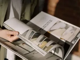 Hands flipping through a glossy fashion magazine on a bed or sofa
