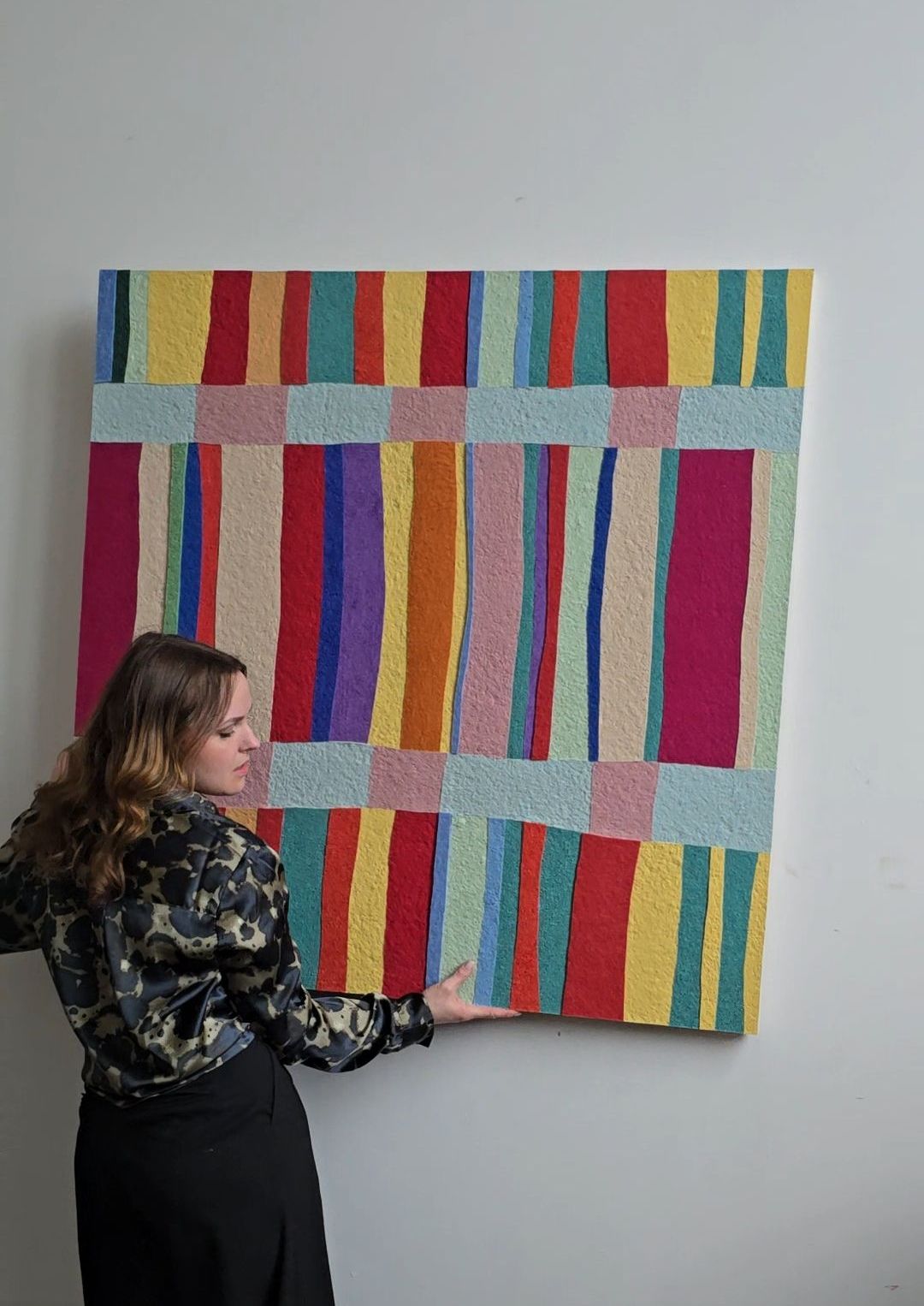 Artist holding a colorful wall art panel made from recycled textile waste and plant-based glue,  bold multi-coloured stripes