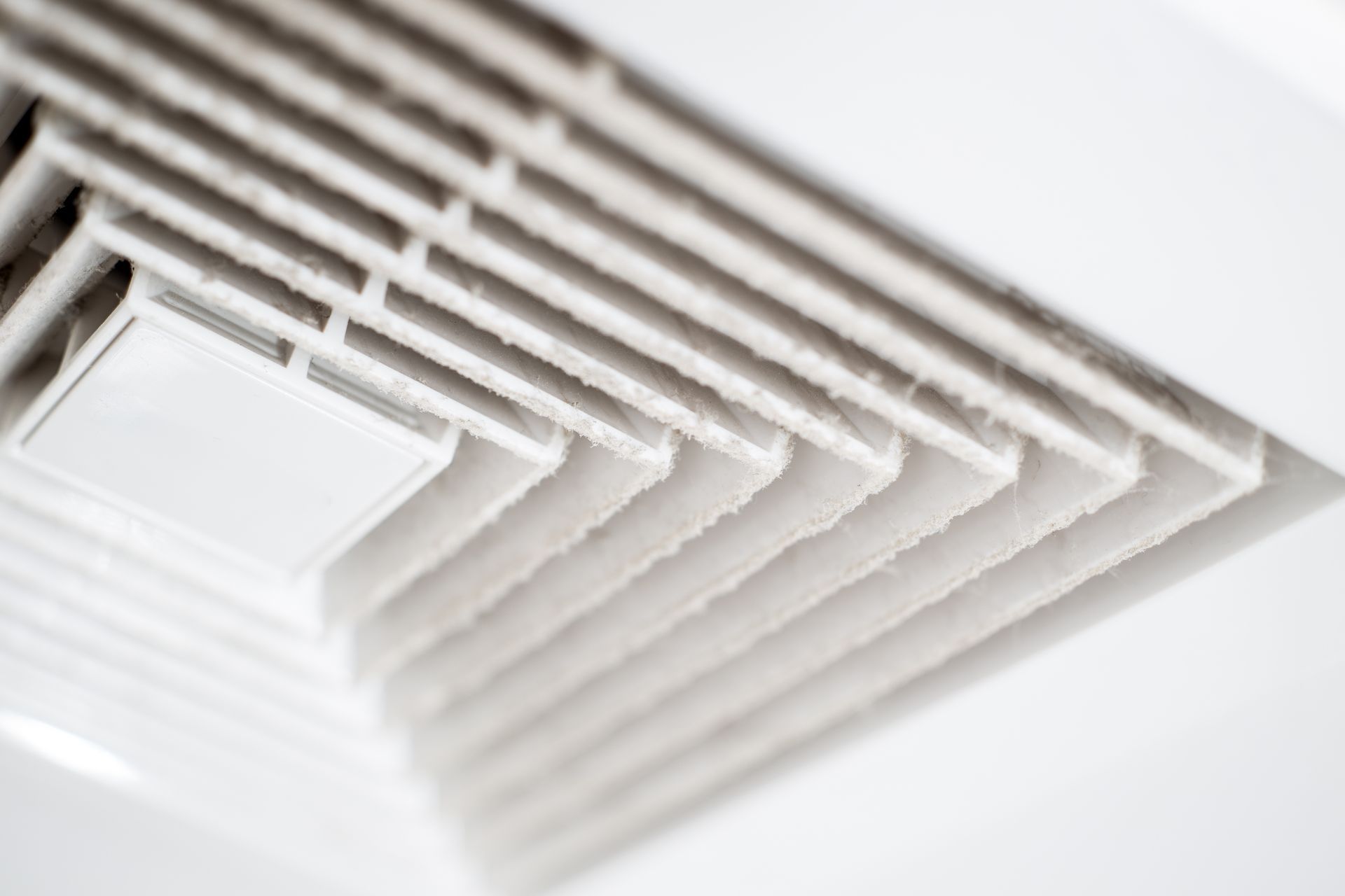 Close-up of a white ceiling air vent with angled slats and a small control tab