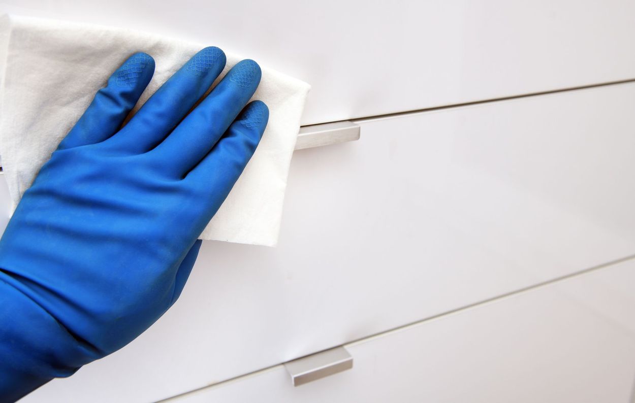 Blue-gloved hand wiping a white cabinet with a cloth