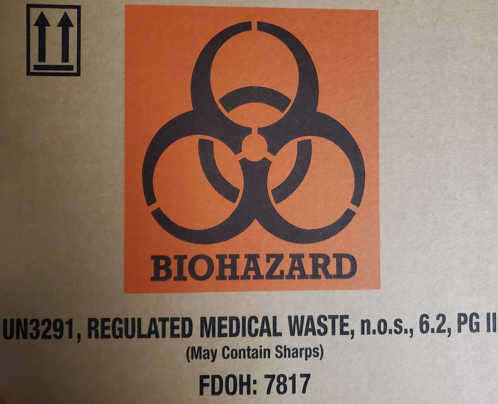 Person in blue gloves holds a red biohazard waste bag in a clinical setting.