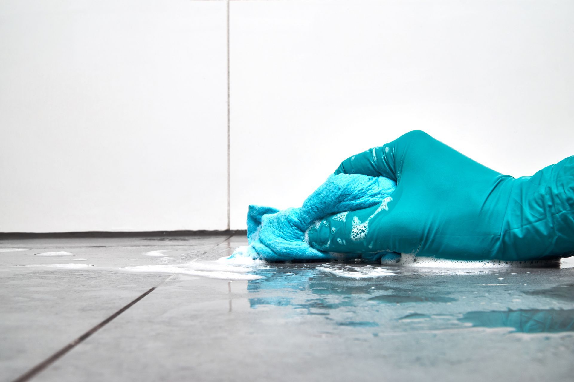 Gloved hand wiping liquid spill from tiled floor with a blue cloth