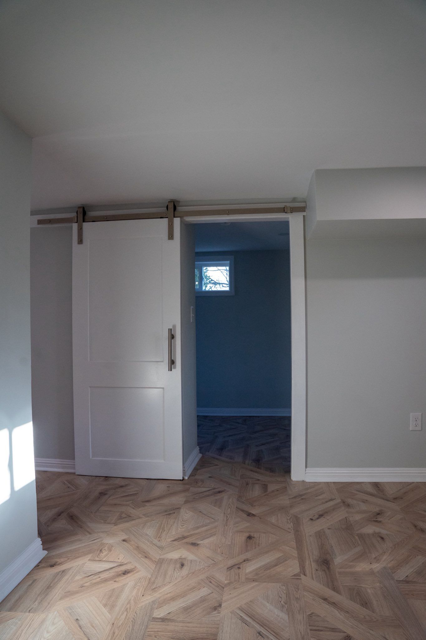 A room with a white sliding barn door leading to another area, featuring gray walls and patterned wood flooring.