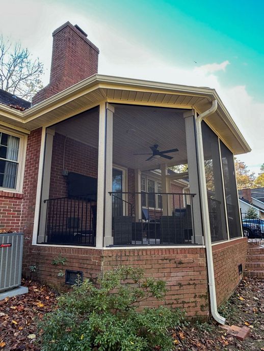 A screened-in porch with a brick foundation and chimney, featuring a ceiling fan and patio furniture.