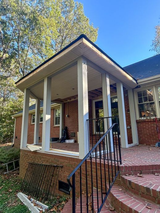 A brick house with a covered porch featuring white wooden pillars, a black metal railing, and brick stairs.