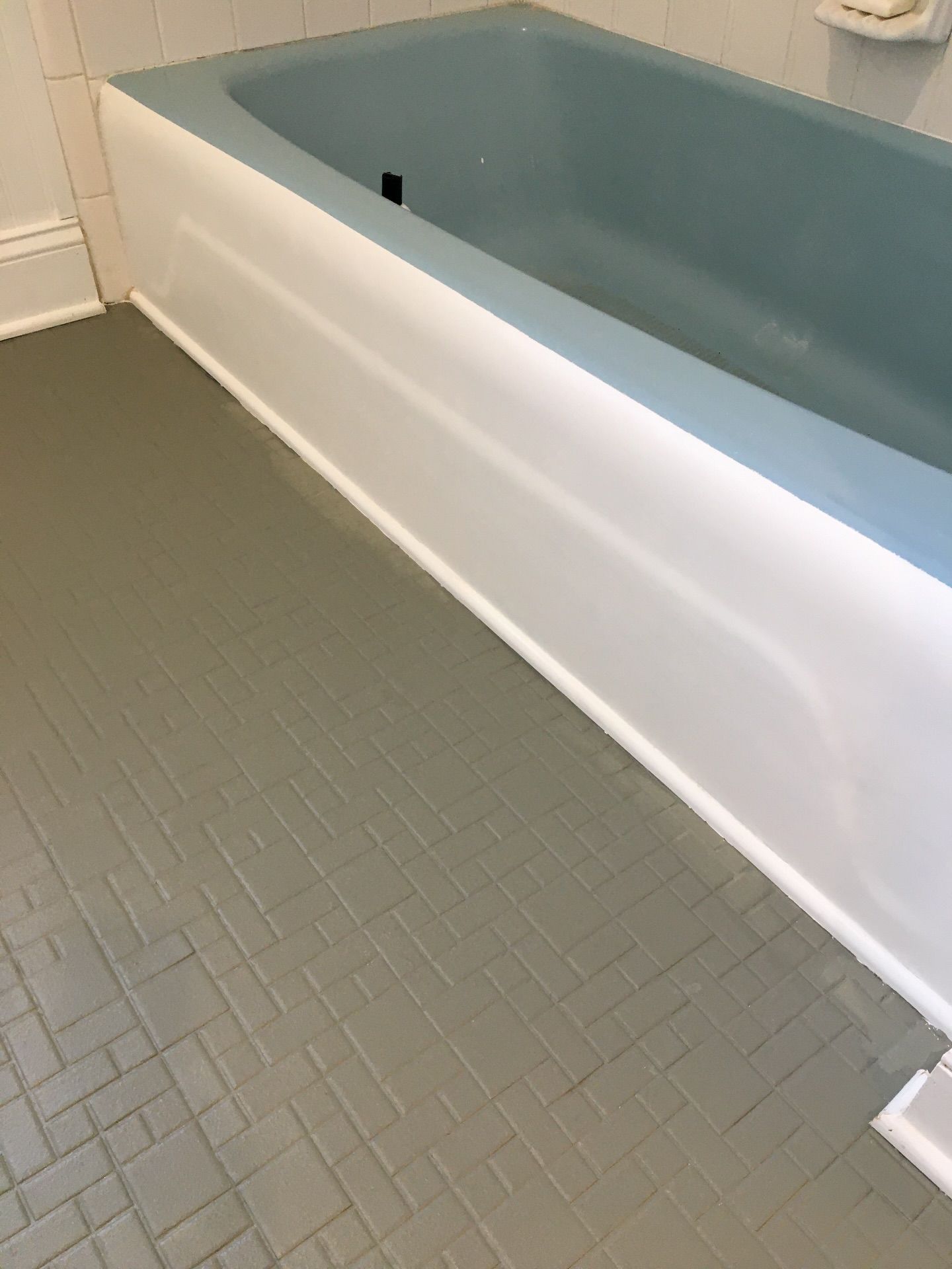 A white bathtub with a blue interior sits next to gray tile flooring in a bathroom.