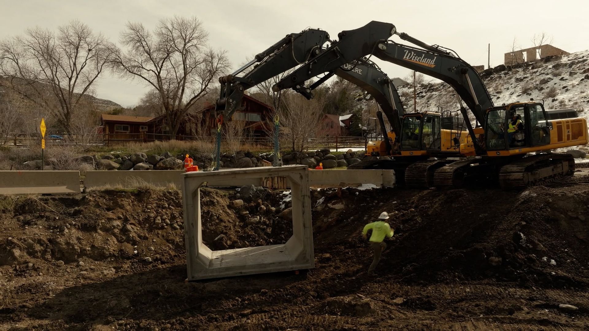 Excavator demolishing a concrete structure at a muddy construction site, with workers nearby