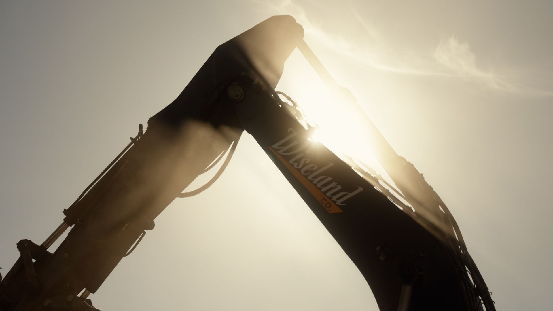 Silhouette of an excavator arm against a bright sun and hazy sky