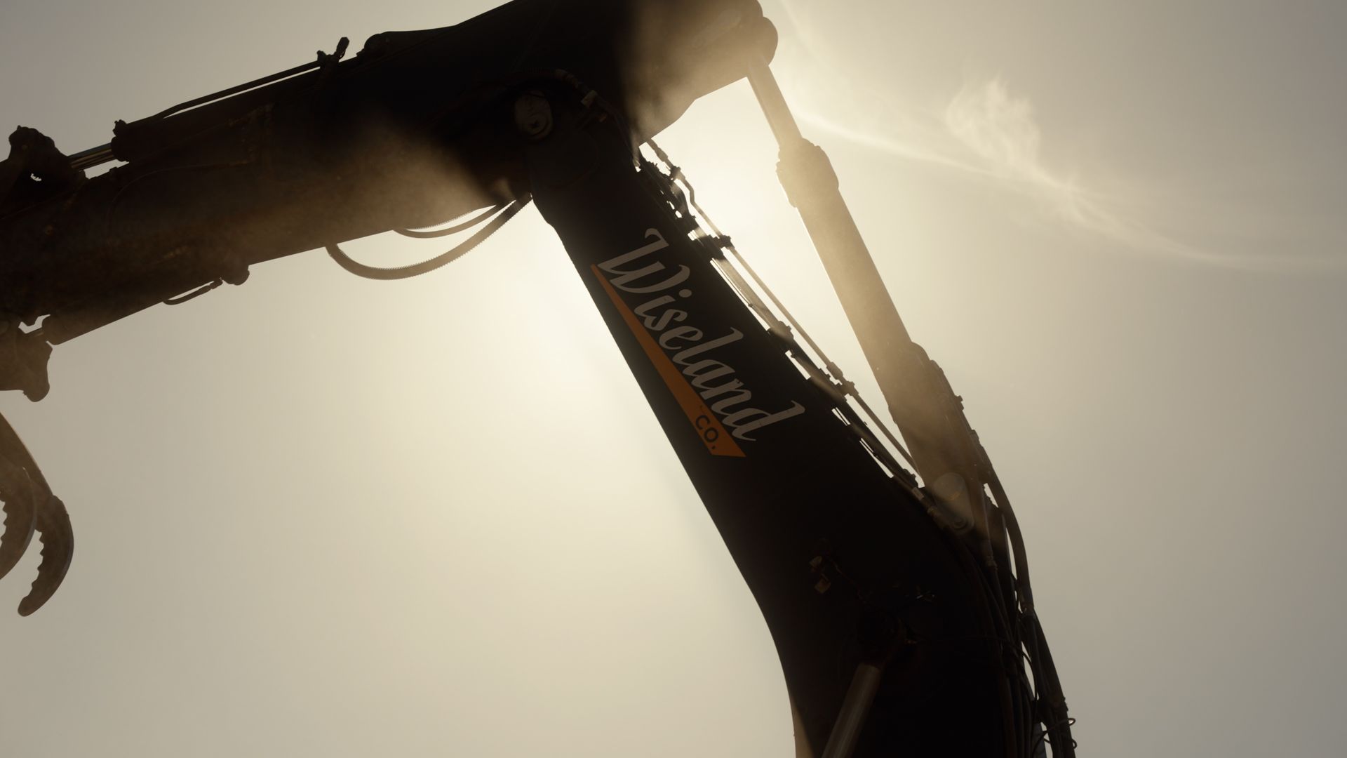 Silhouetted construction excavator arm against a bright sunlit sky