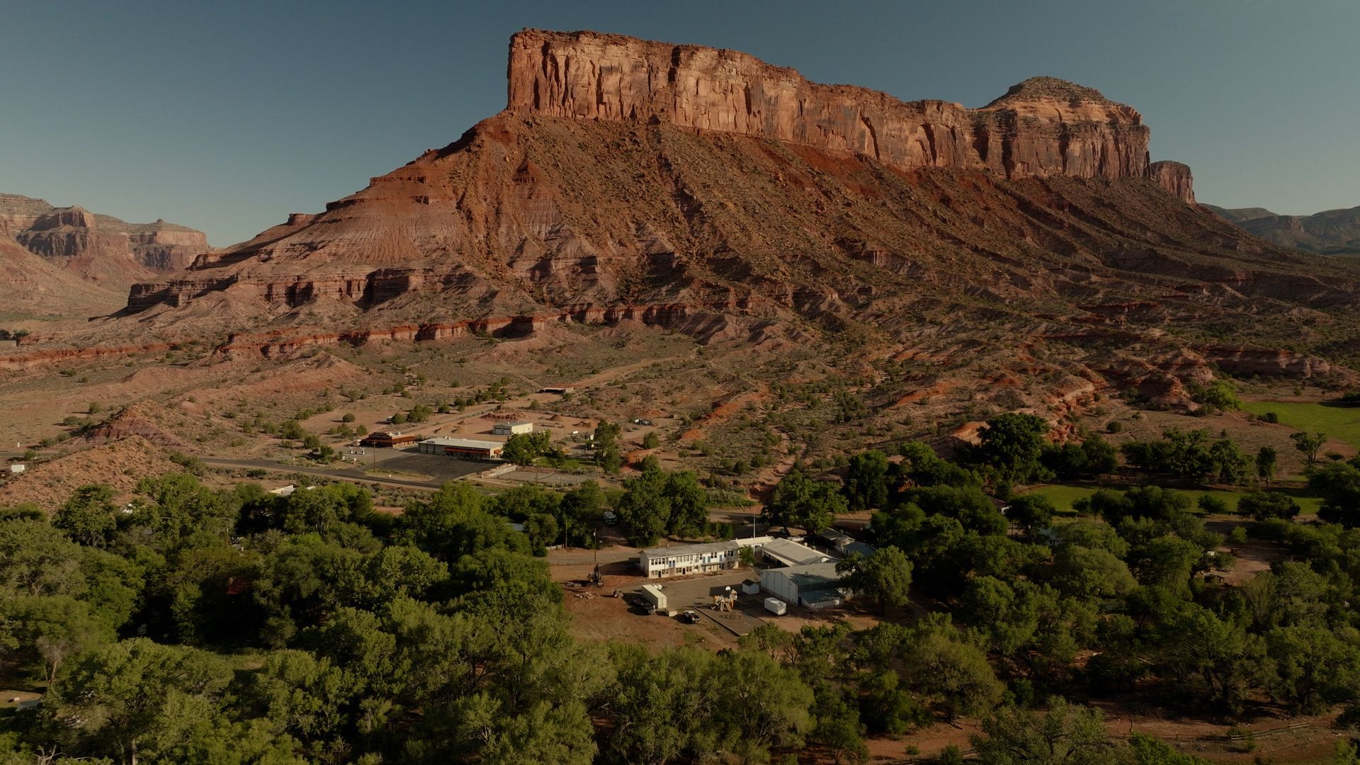 Red sandstone mesa above a green desert valley with scattered homes under a clear sky