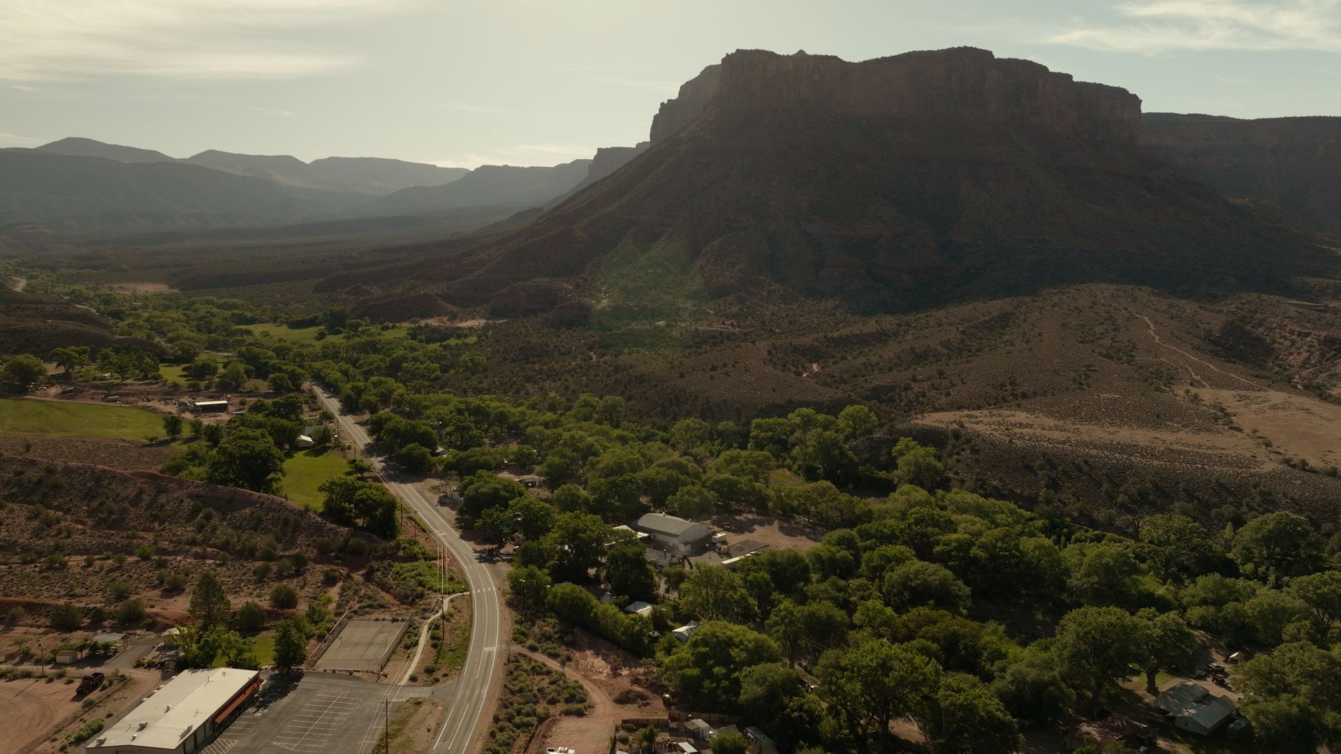 A winding road through a green valley beneath a large flat-topped mountain at sunset.