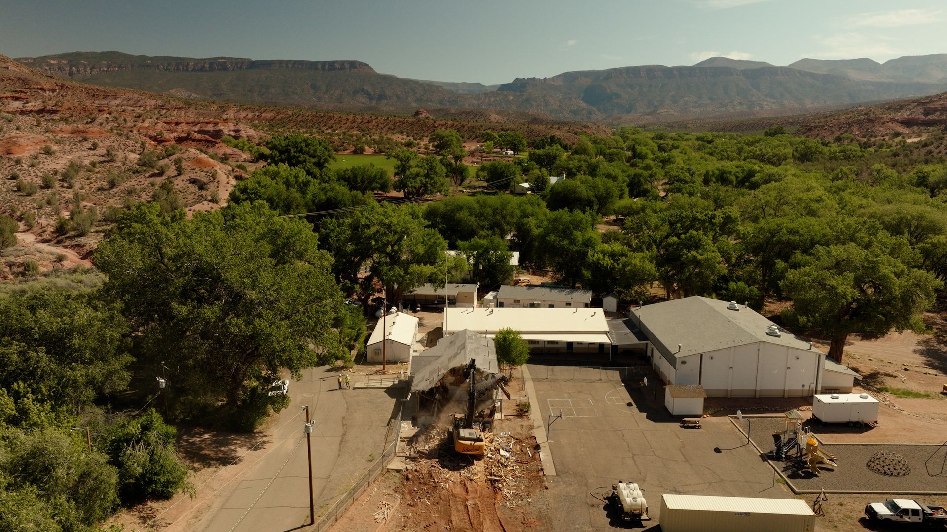 Aerial view of a rural settlement with trees, dirt roads, and low buildings in a rocky valley.