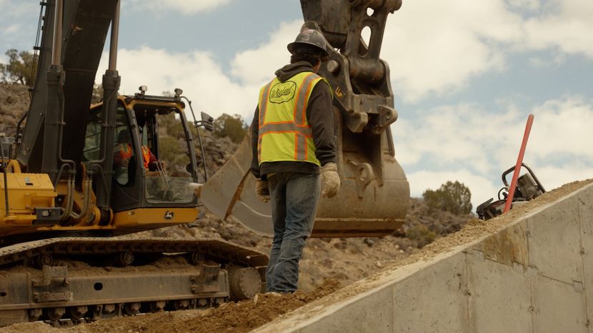 Construction worker guiding excavator bucket at a roadwork site