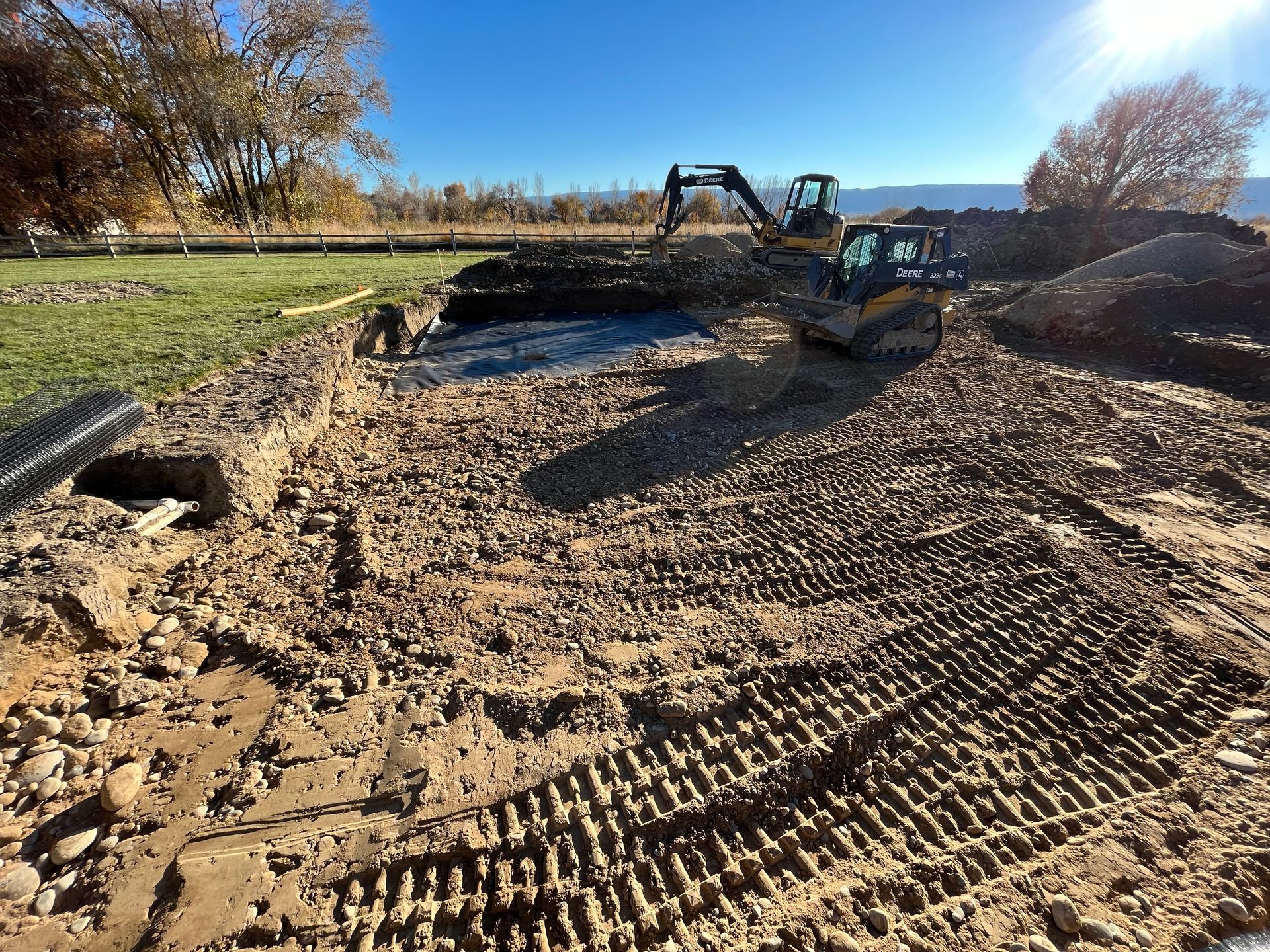 Excavator clearing dirt at a muddy construction site under a blue sky