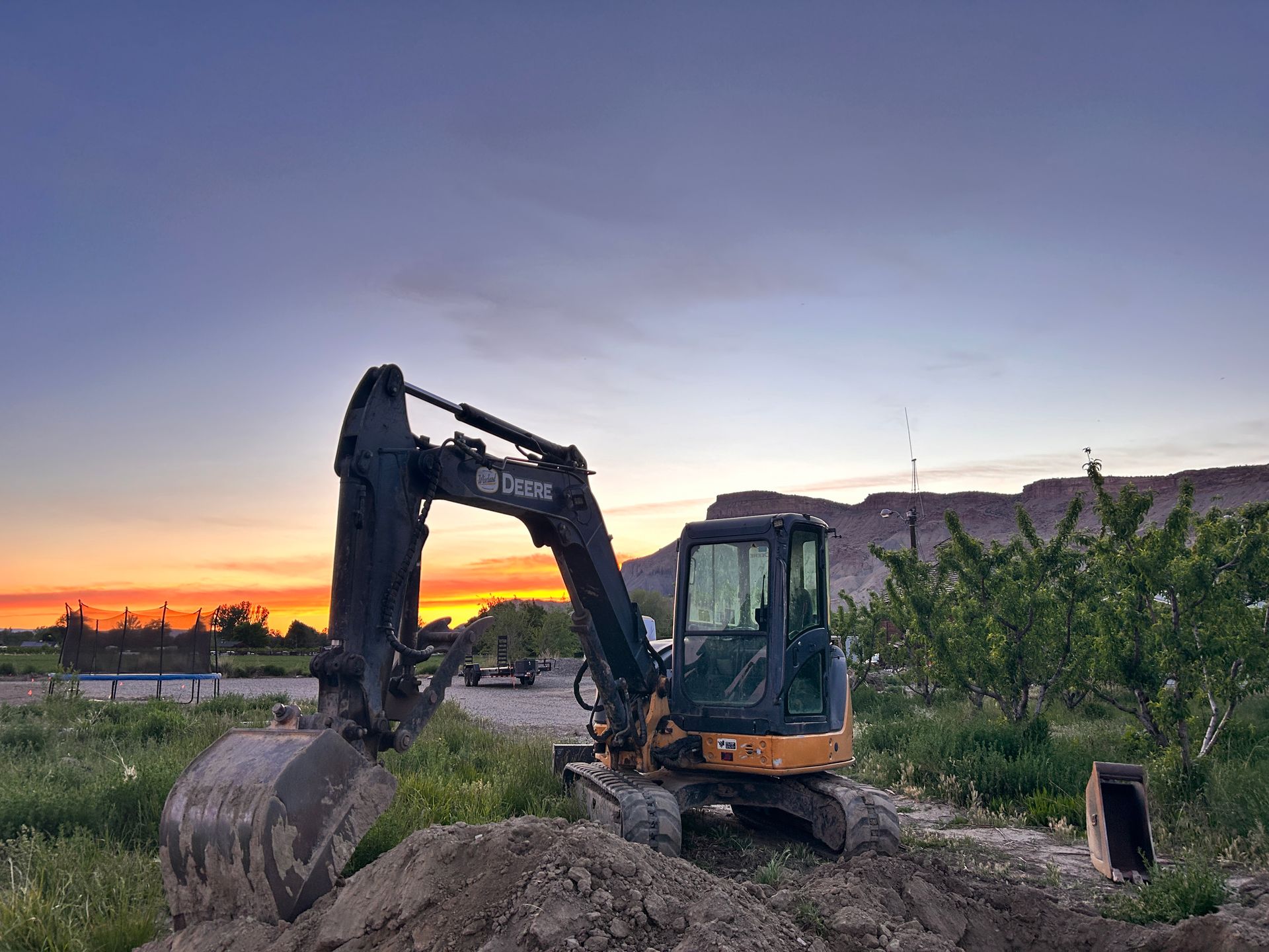 An excavator is digging a hole in a field at sunset.