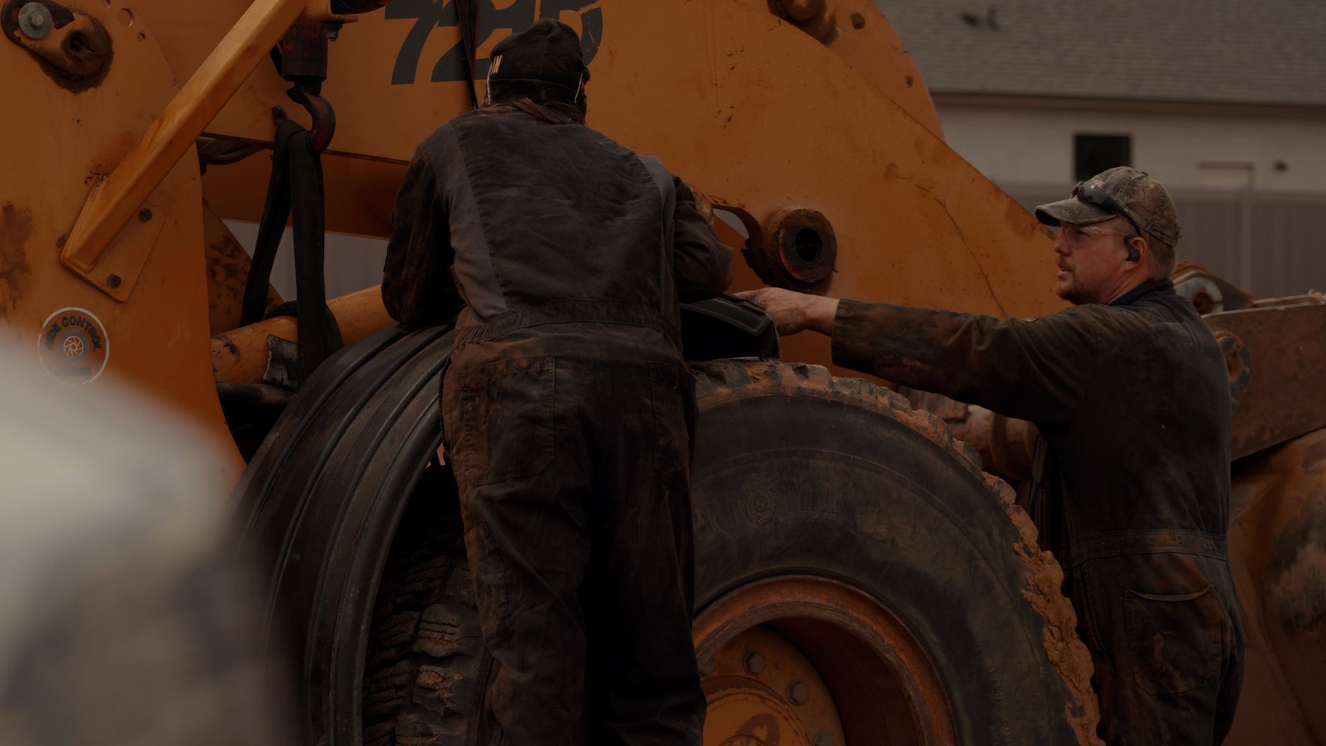 Workers beside a large heavy-duty vehicle tire in an industrial setting