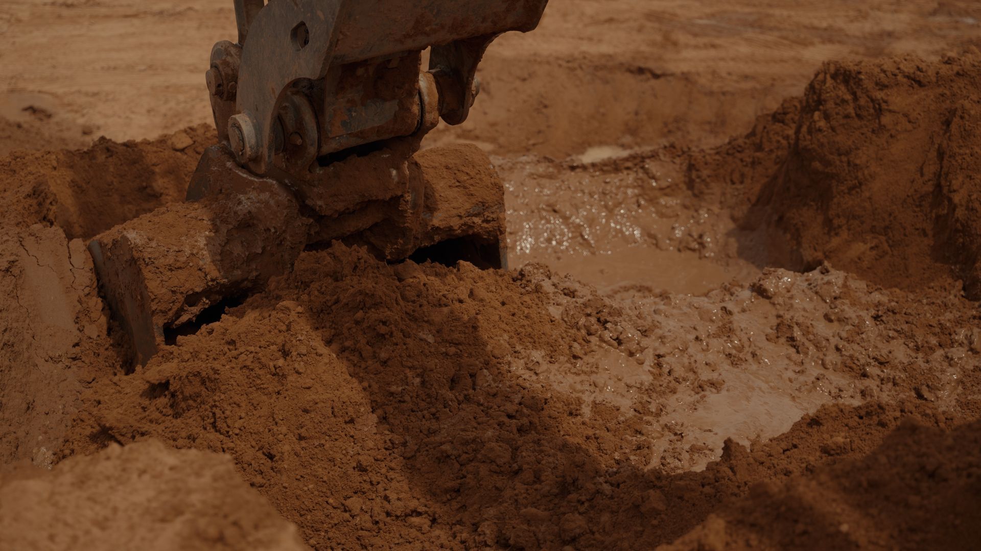 Excavator bucket scooping dirt in a brown earthwork site