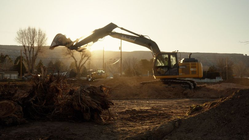 Excavator loading brush on a construction site at sunset.