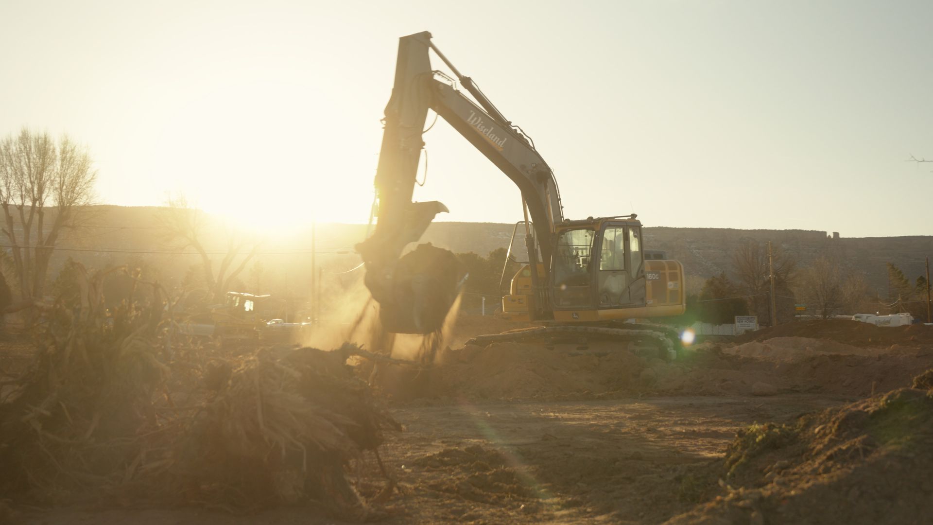 Excavator working at a dusty construction site in warm sunset light
