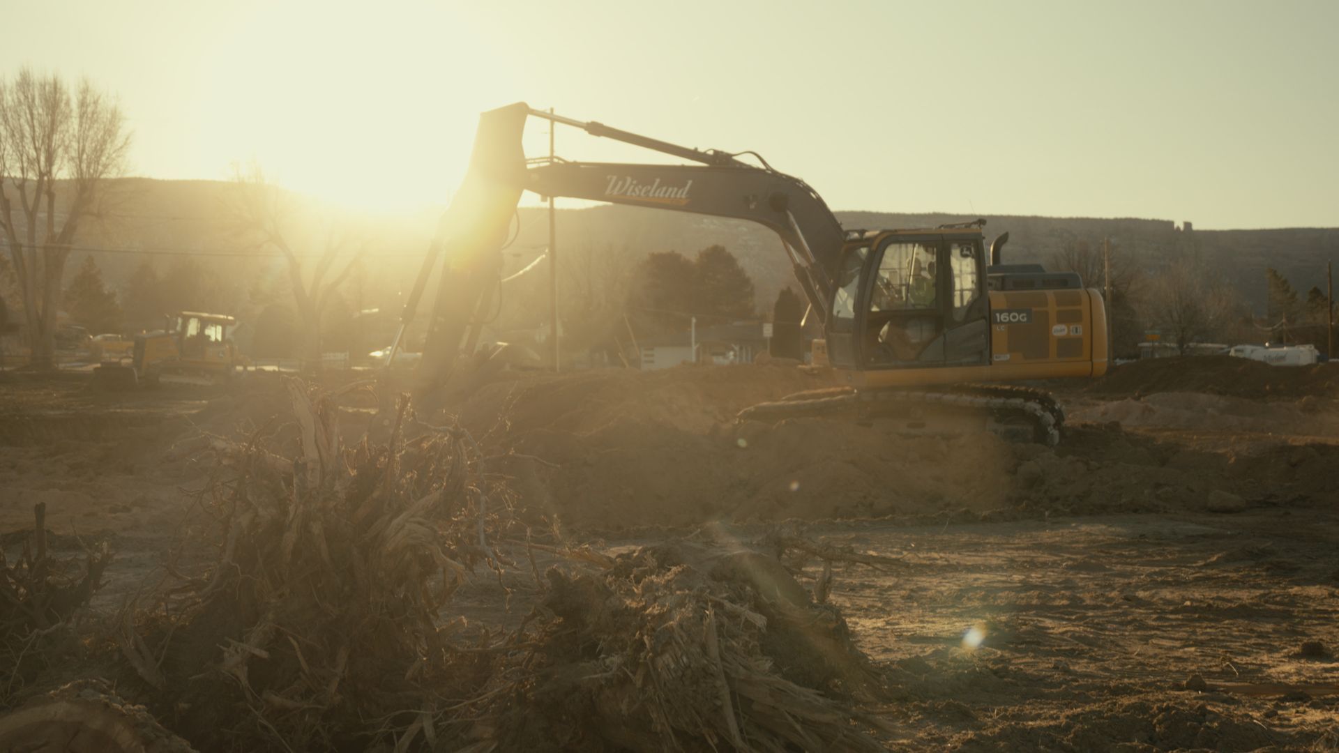 Excavator working on a dusty construction site at sunrise, with bright sun glare in the background