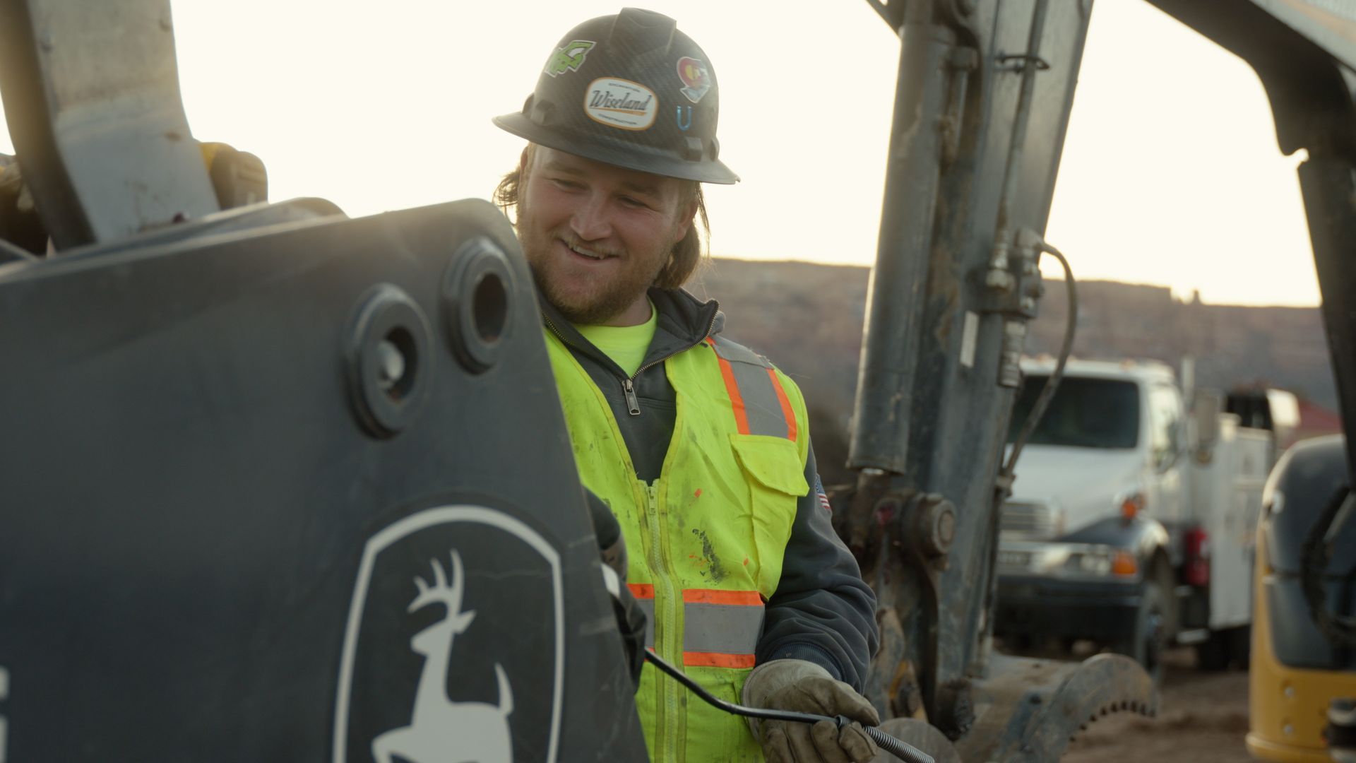 Construction worker in hard hat and hi-vis vest operating machinery outdoors at sunset