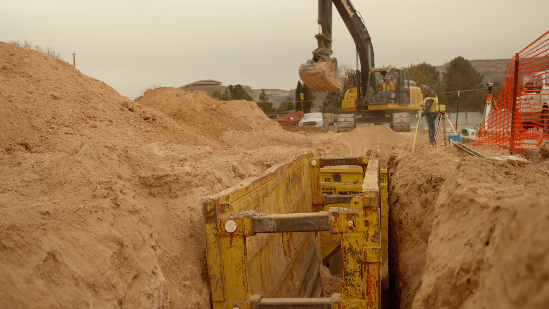 Excavator digging a trench beside a large sand pile at a construction site