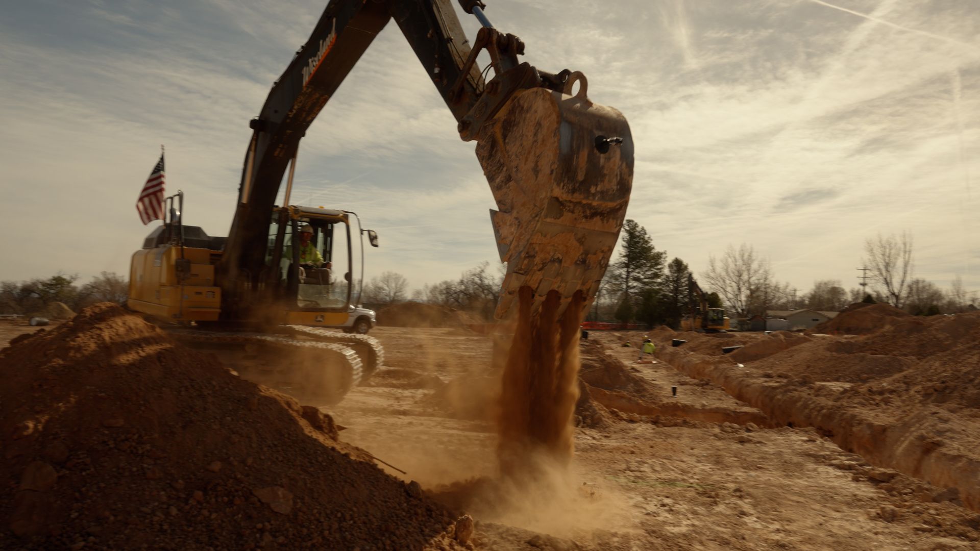Excavator dumping dirt at a construction site under a cloudy sky