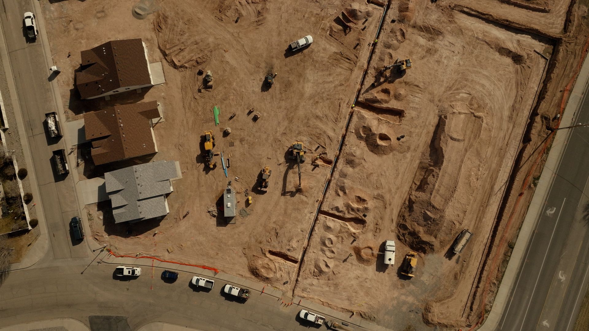 Aerial view of a dusty construction site with excavators, trucks, and nearby roads.