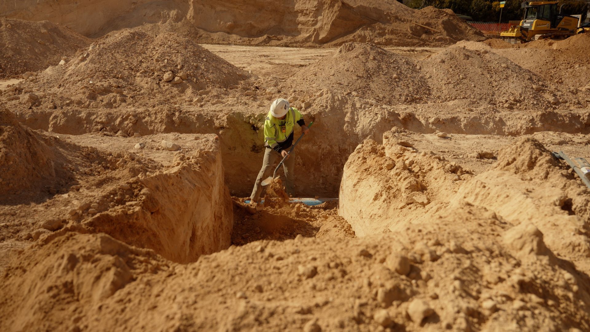 Worker in a yellow vest digging in a large sandy excavation site