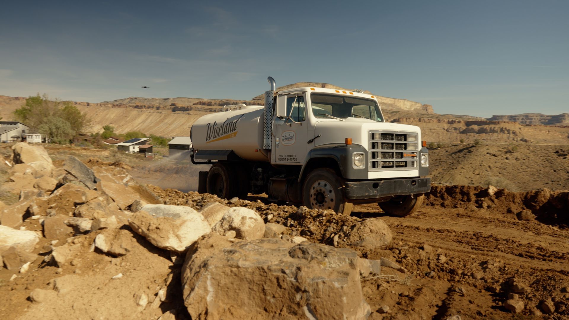 White dump truck driving through a rocky dirt quarry under a clear sky