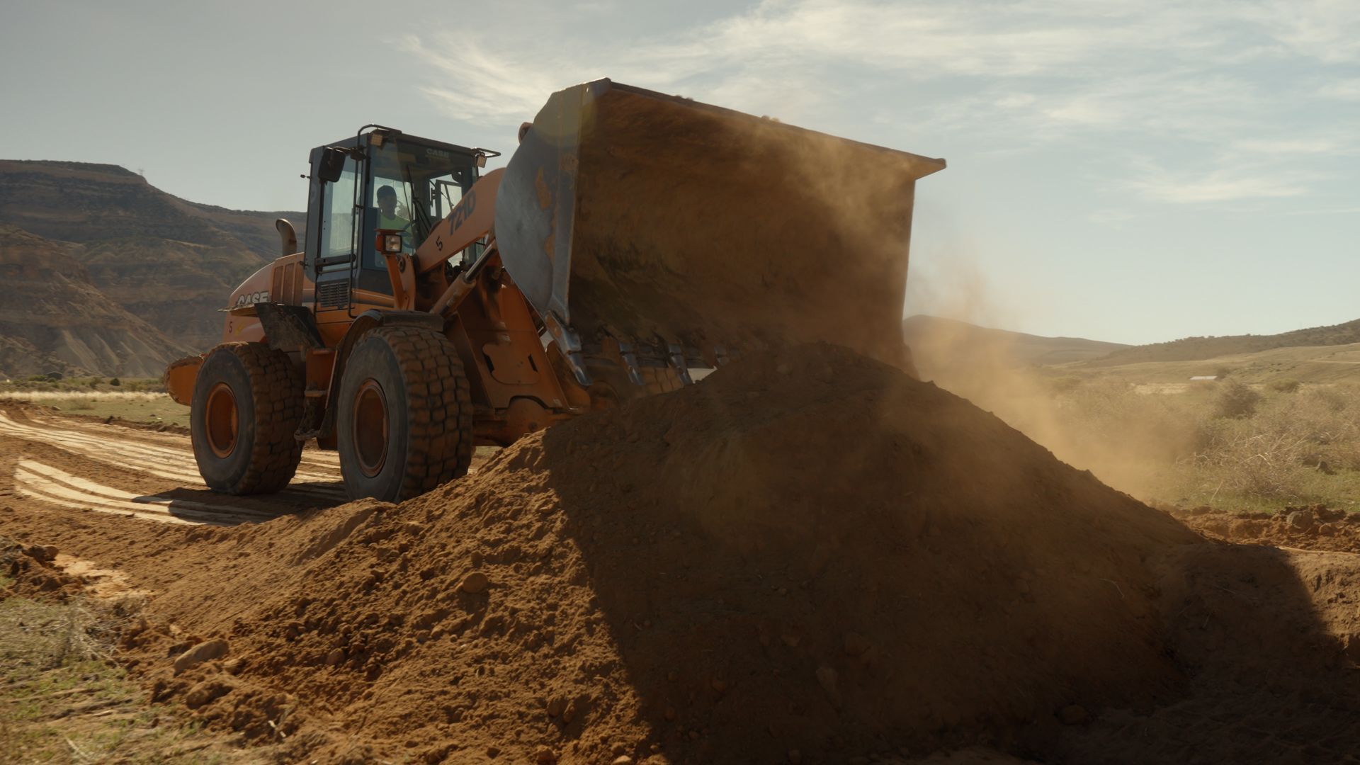 Orange bulldozer dumping dirt in a dry, sandy landscape at sunset