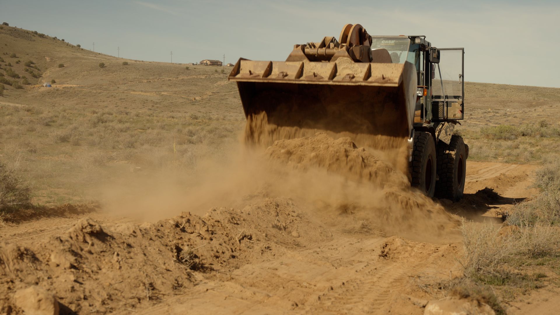Bulldozer dumping dirt across a dusty desert road, raising a cloud of dust