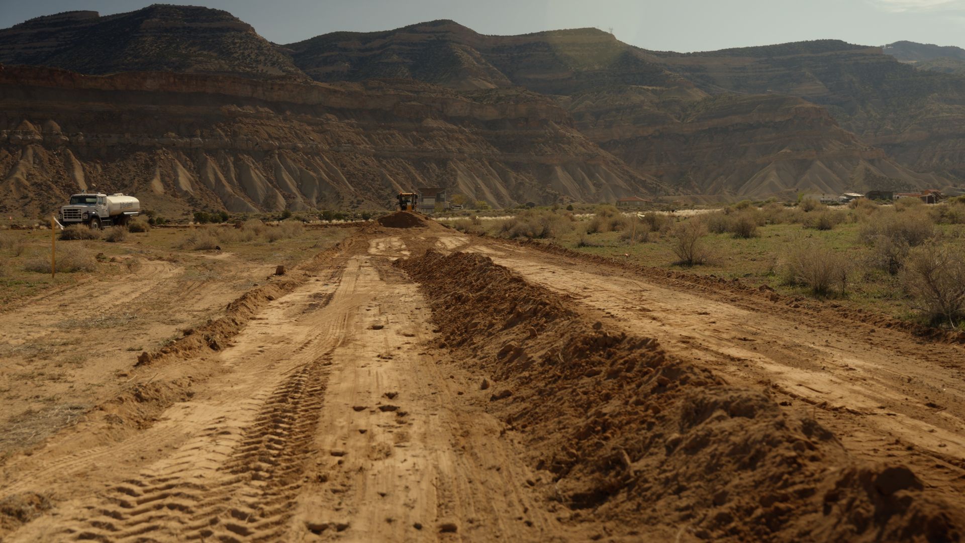 Dirt road under construction in a desert valley with mountains in the background