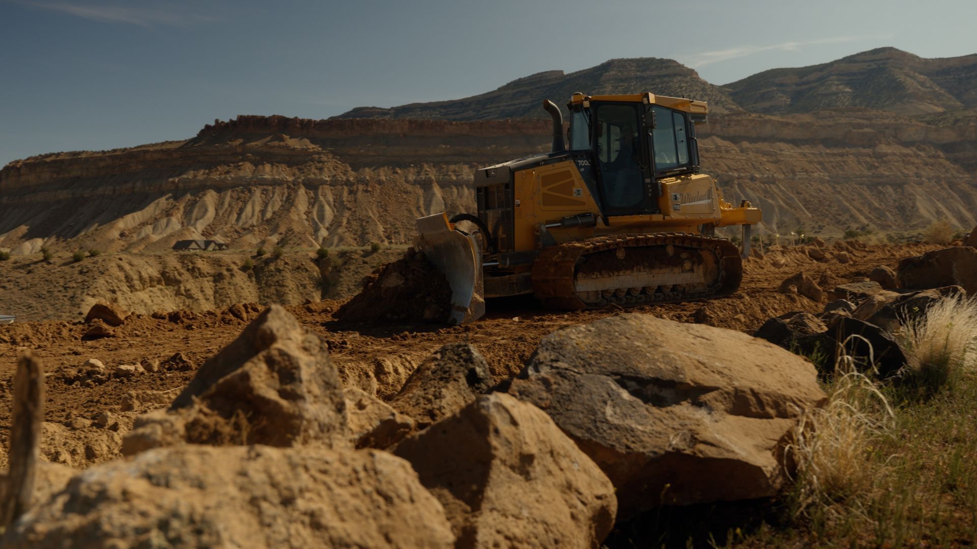 Yellow bulldozer clearing rocky dirt in an open quarry with mountains in the background