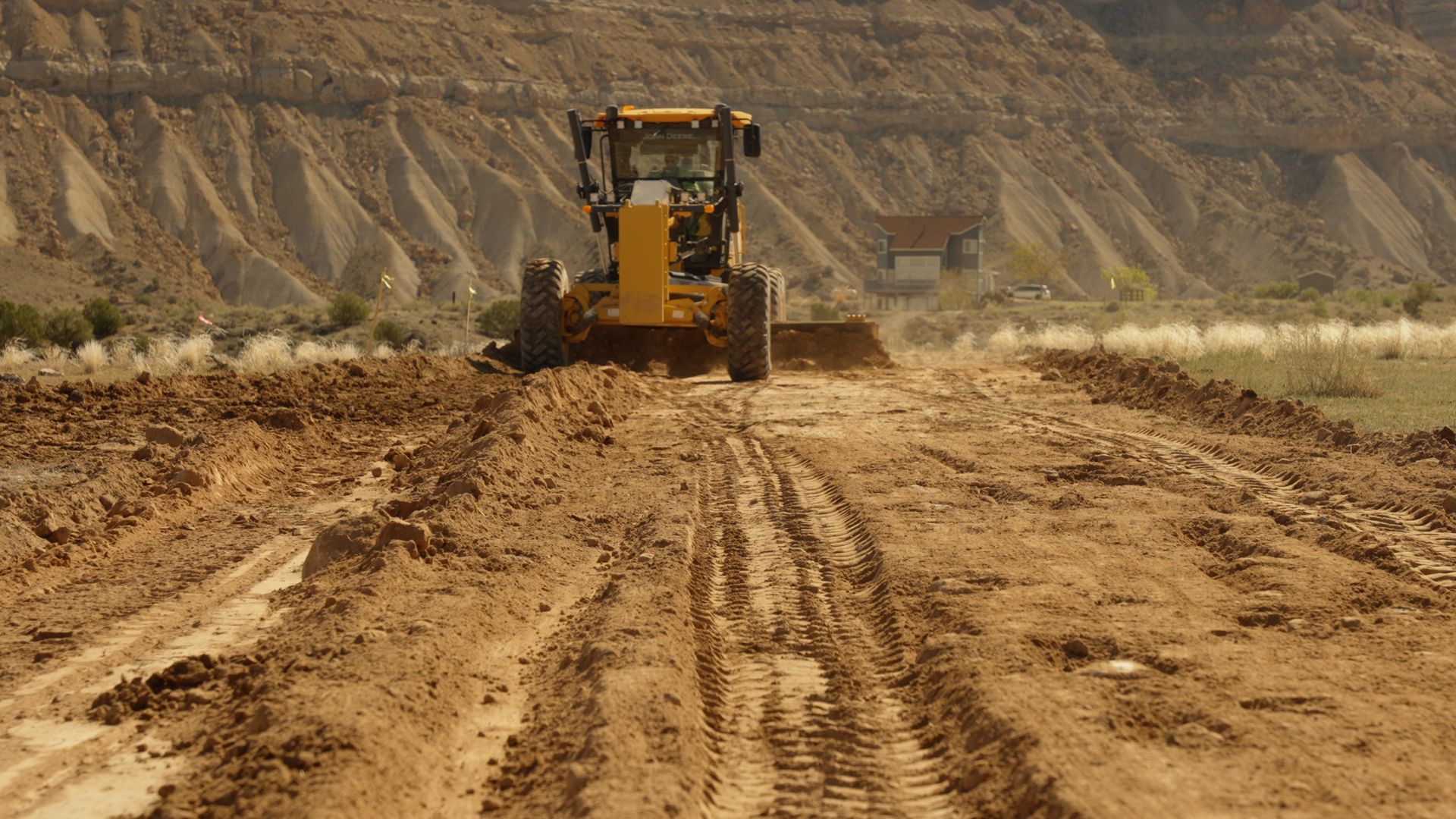 Yellow bulldozer grading a muddy dirt road in a desert landscape