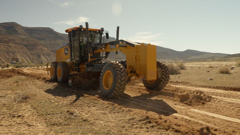 Yellow road grader working on a dirt road in a dry desert landscape