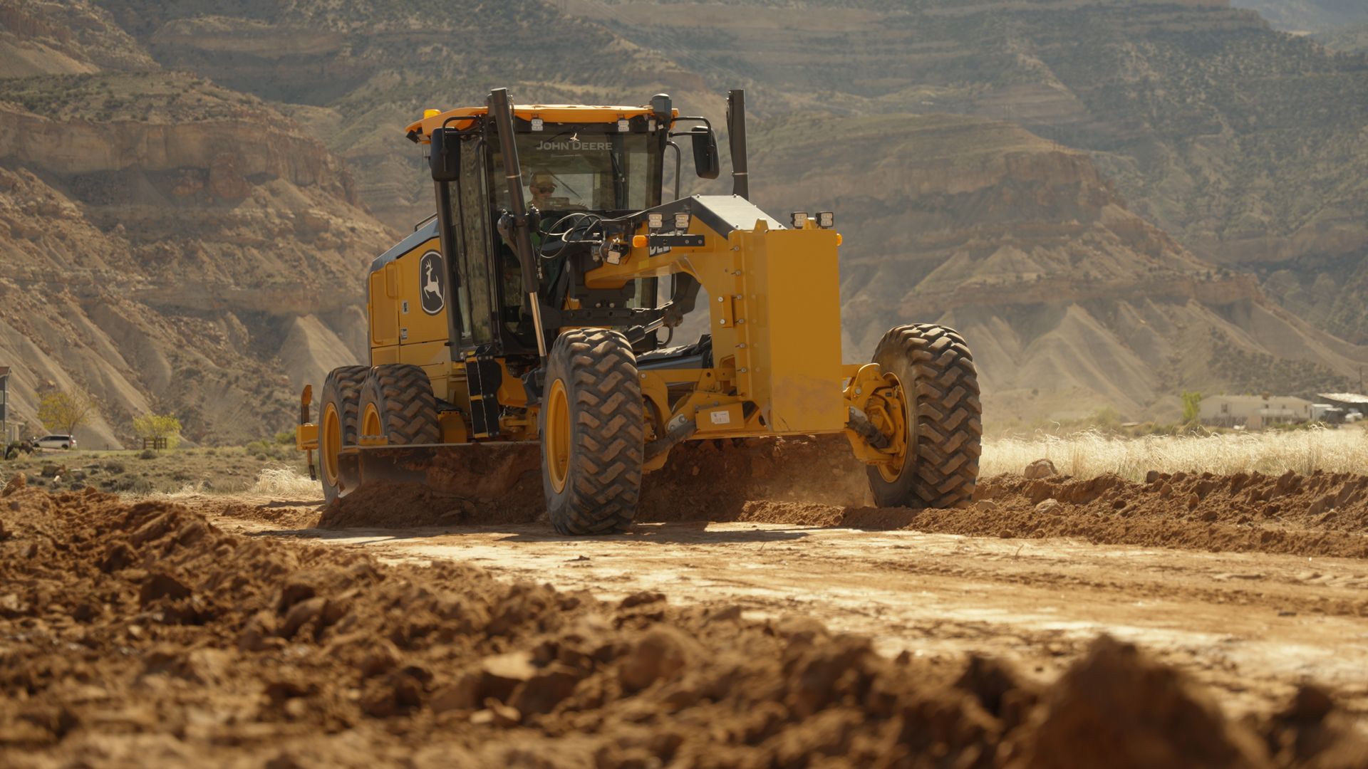 Yellow road grader smoothing a dirt road in a dusty rocky construction site