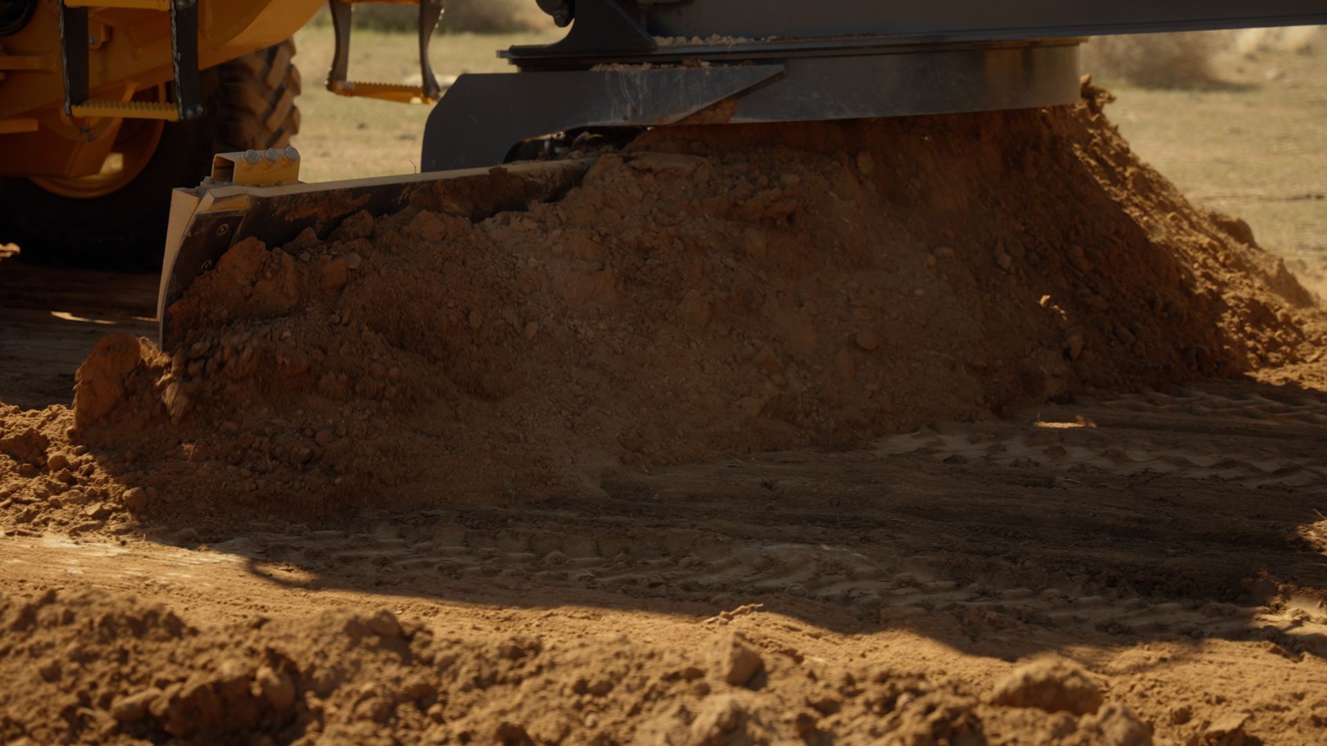 Bulldozer pushing a large pile of dirt on a dusty construction site