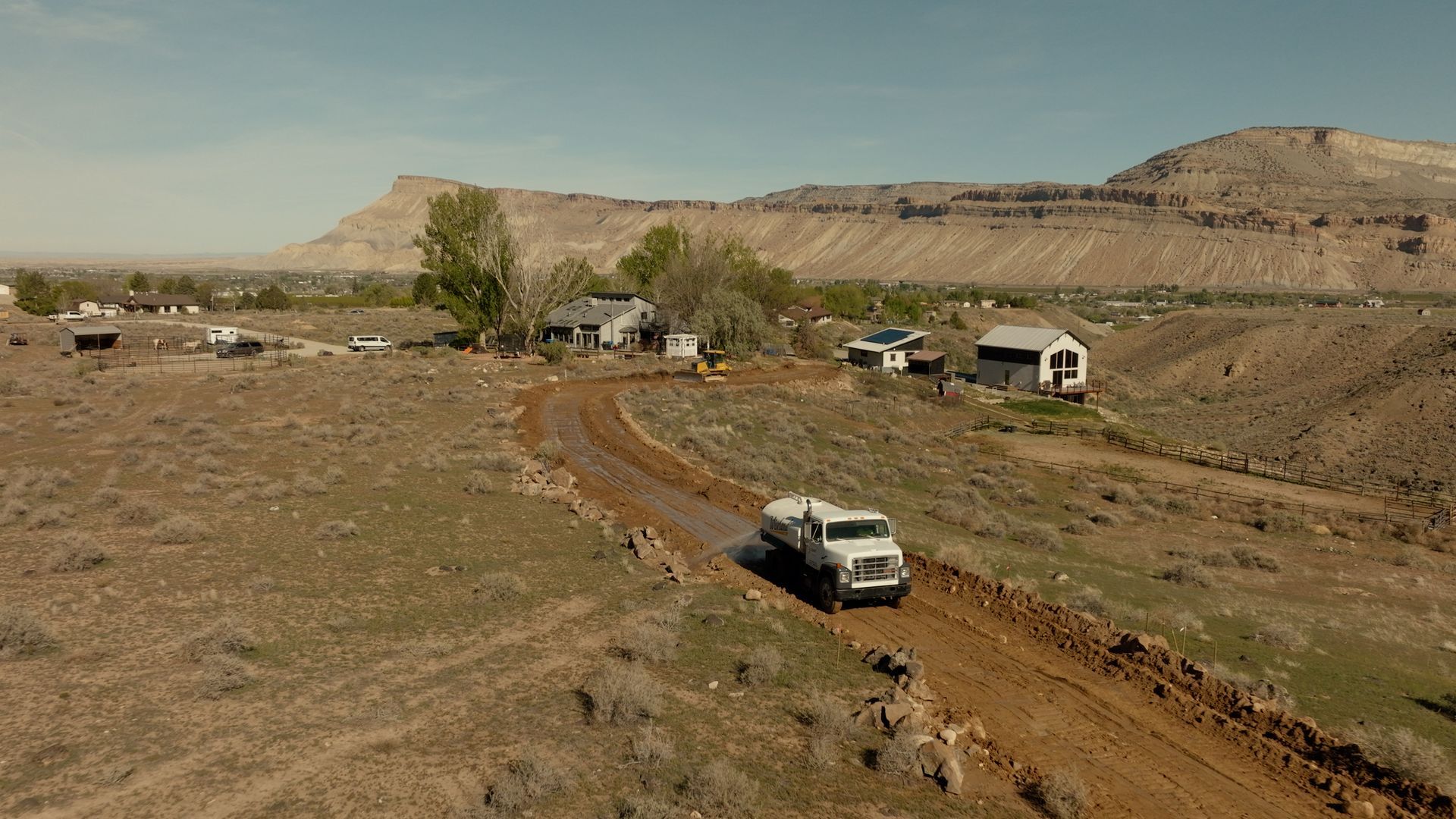 Off-road vehicles on a dirt track through a dry desert landscape with hills in the background