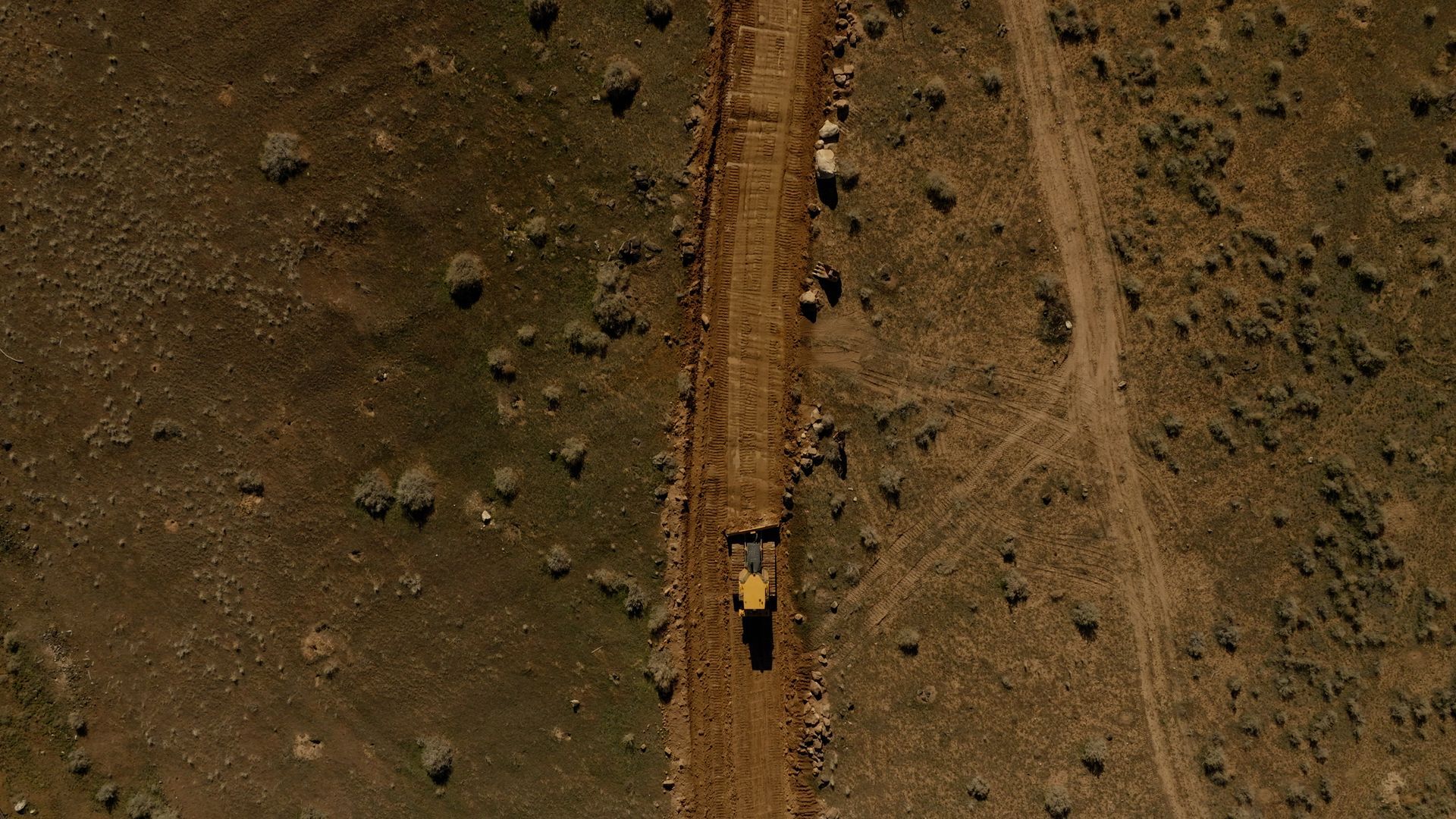 Aerial view of a yellow truck on a dirt road through dry, rocky terrain.