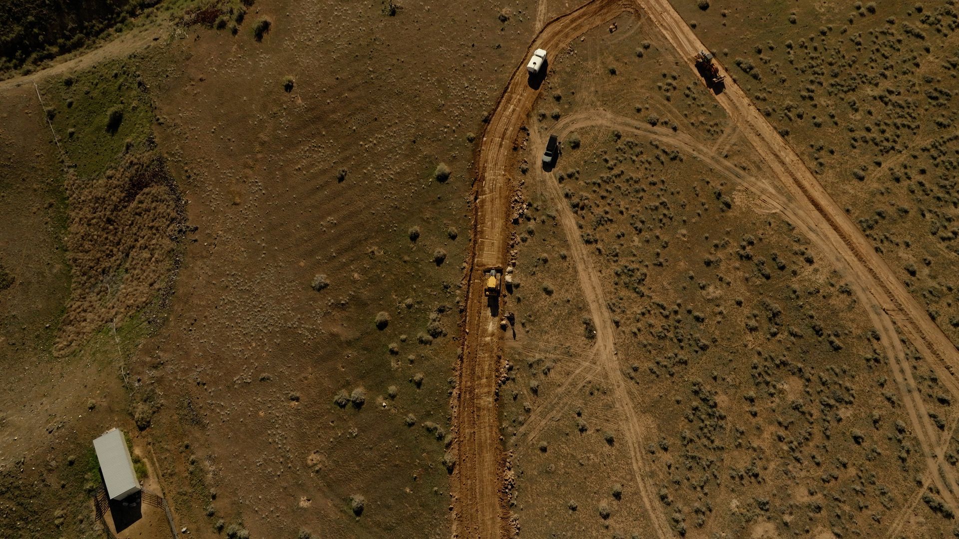 Aerial view of a dirt road winding through dry hills, with several vehicles traveling along it.