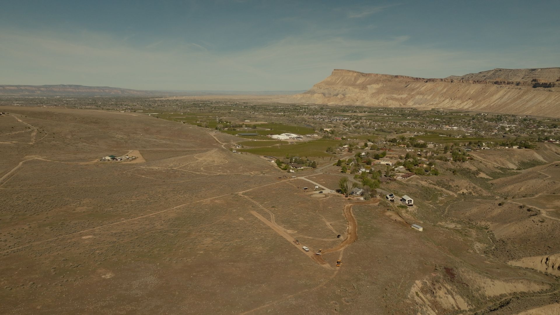 Arid canyon landscape with rocky plains, a green valley, and distant mesa under a clear sky