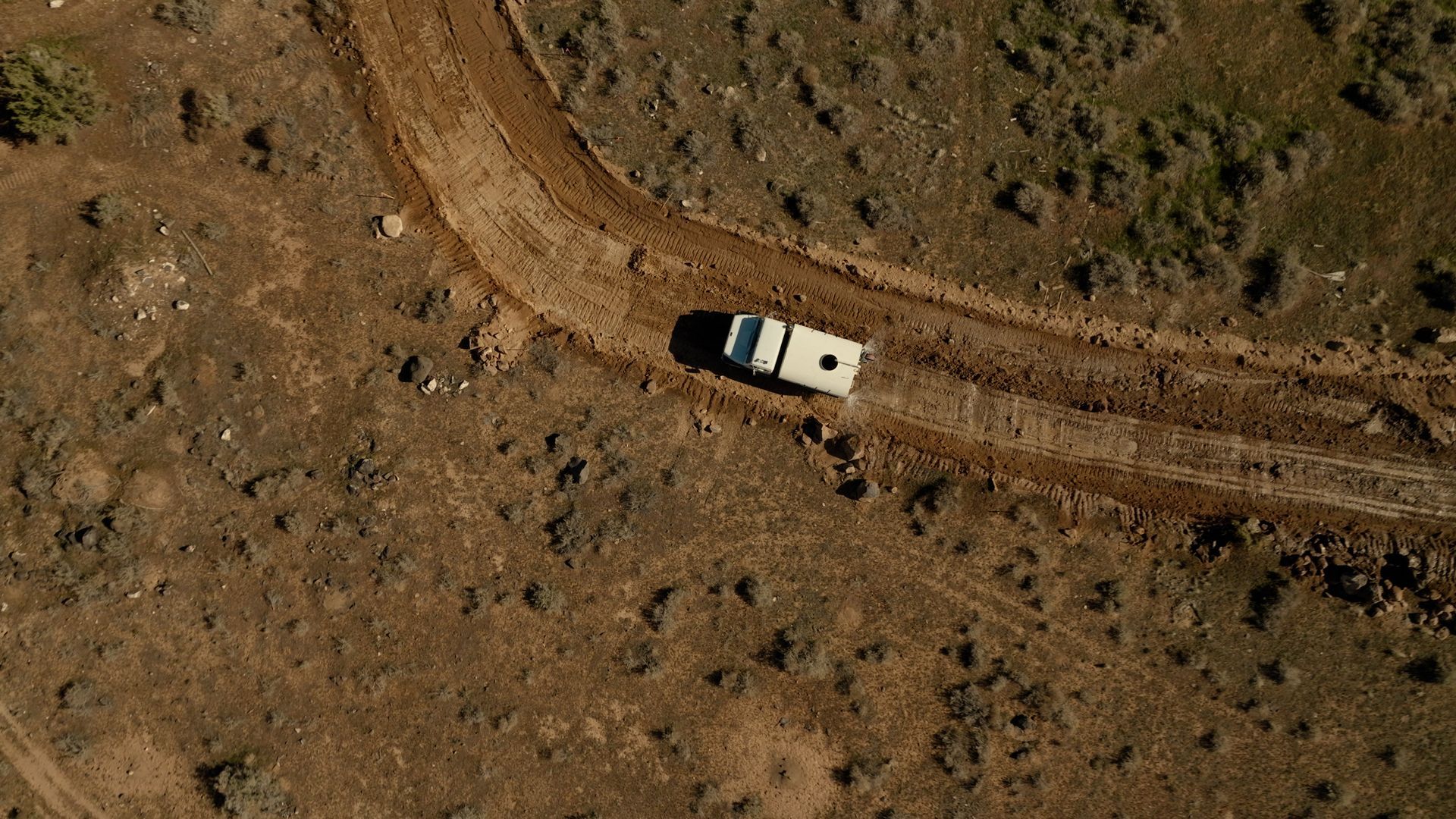 White SUV on a dirt road in a dry, rocky landscape, viewed from above.