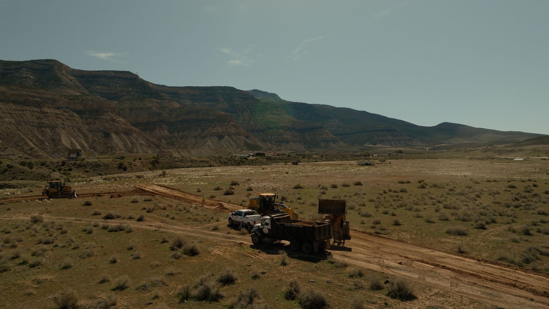 Two off-road vehicles on a dirt track in a dry desert valley beside low mesas