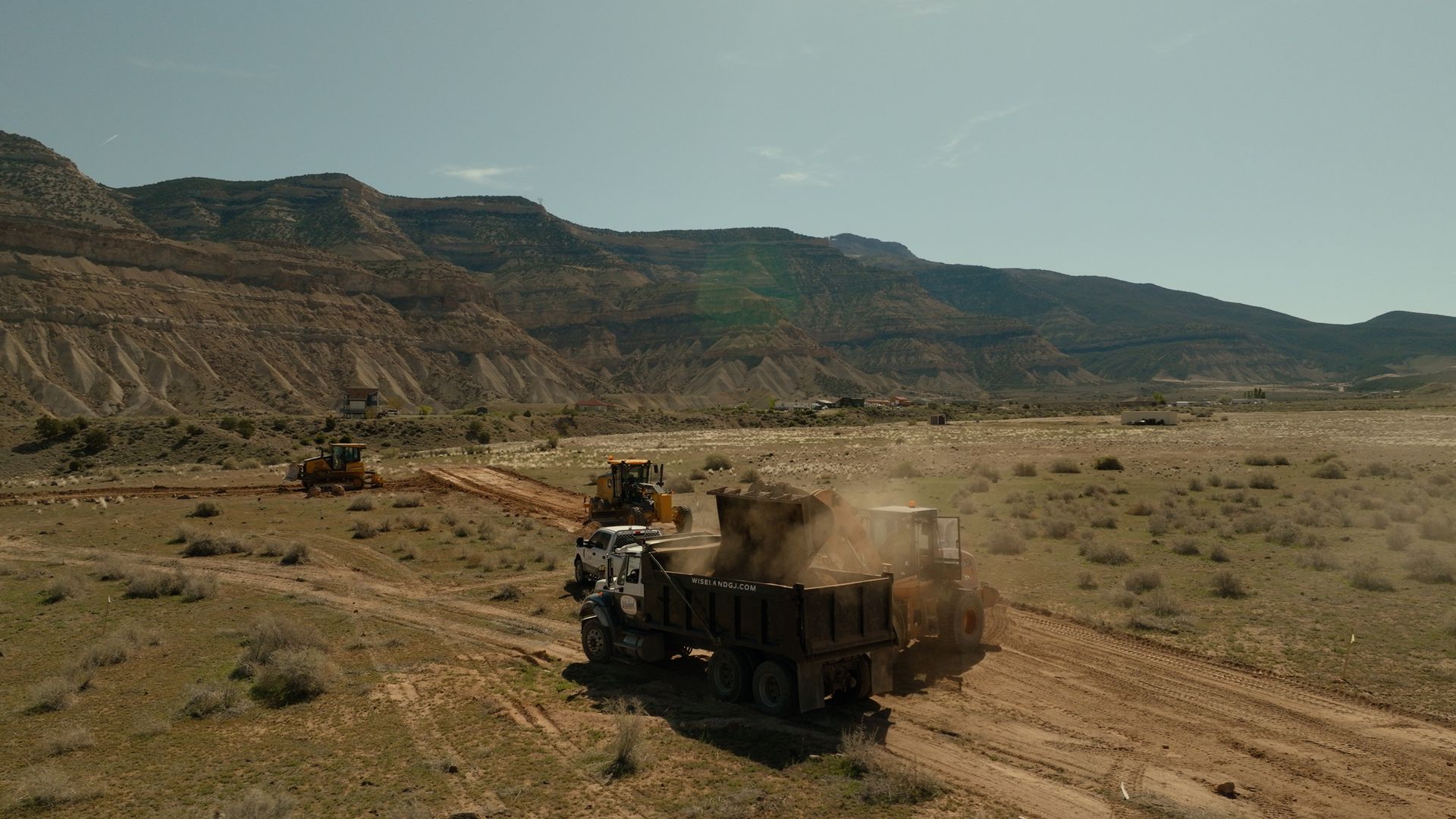 Dusty truck driving on a dirt road through a desert valley with mesas in the background