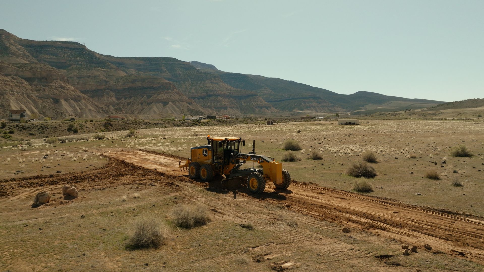 Yellow construction vehicle on a dirt road in a rocky desert valley with mountains in the background