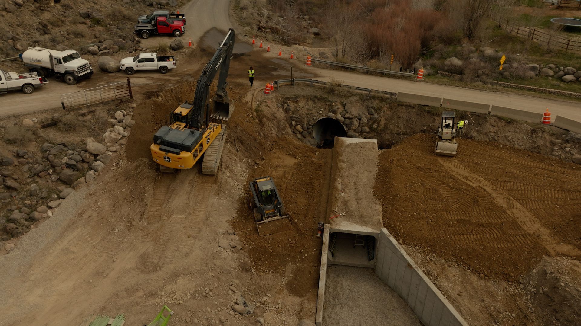 Construction site with excavator digging earth near a concrete structure and parked vehicles nearby
