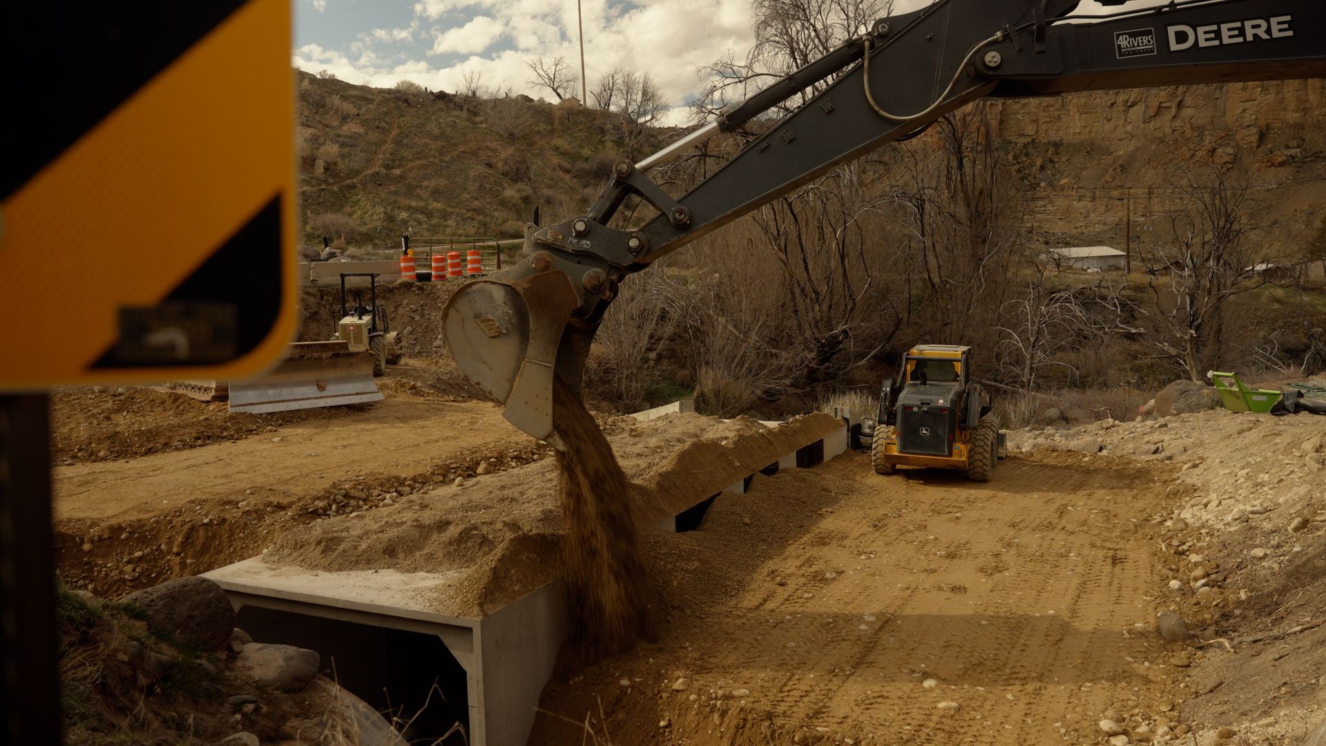 Excavator unloading dirt into a dump truck at a construction site on a wooded hillside