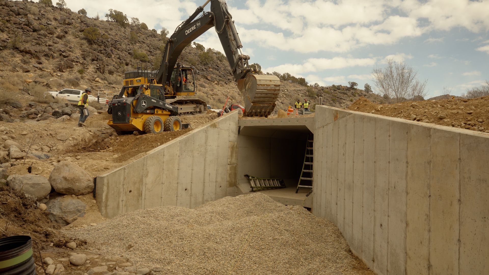 Excavator and loader at a construction site, building a concrete culvert tunnel in a dirt excavation