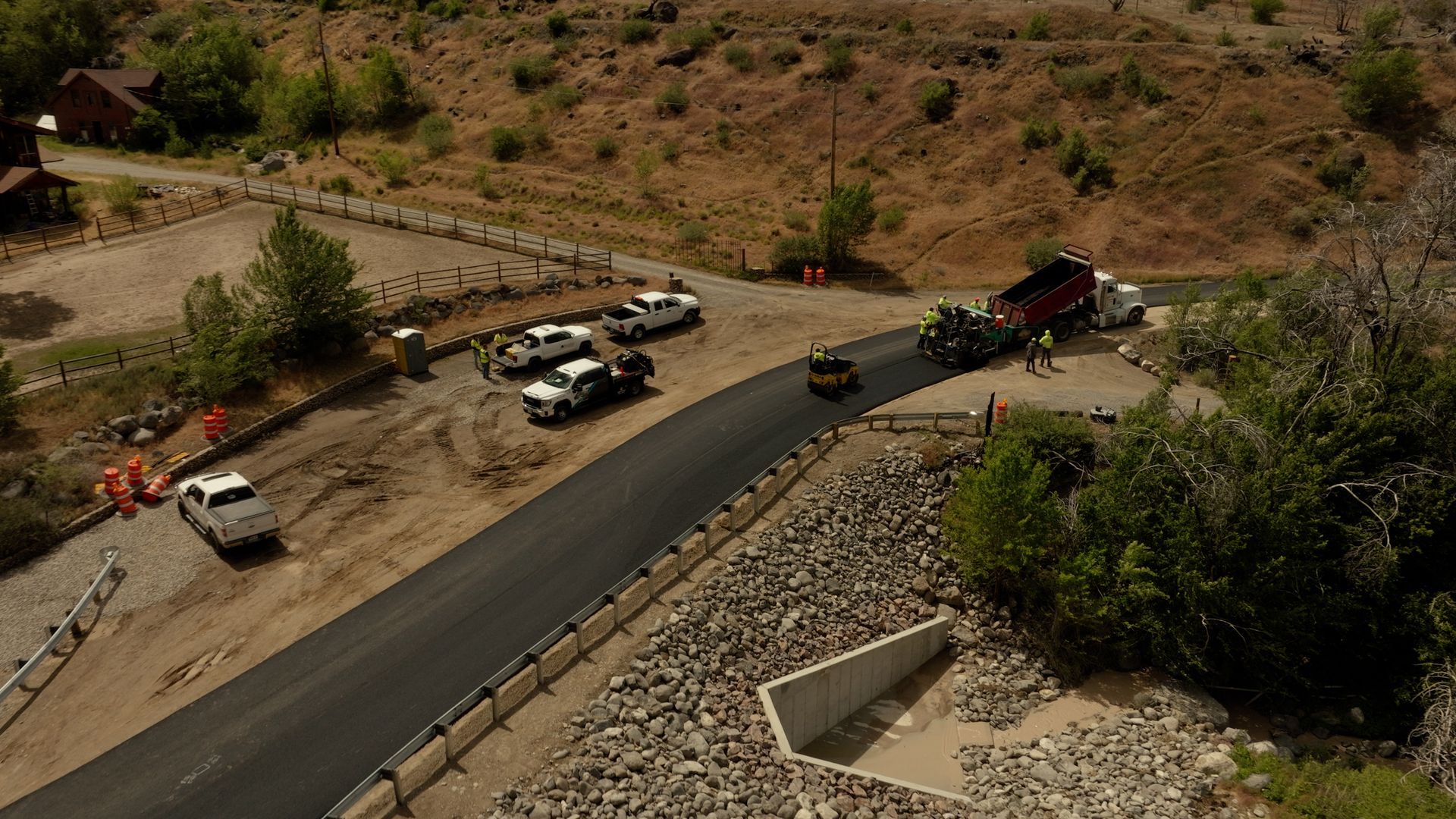 Roadwork on a desert hillside road with several vehicles, construction equipment, and a paved curve.